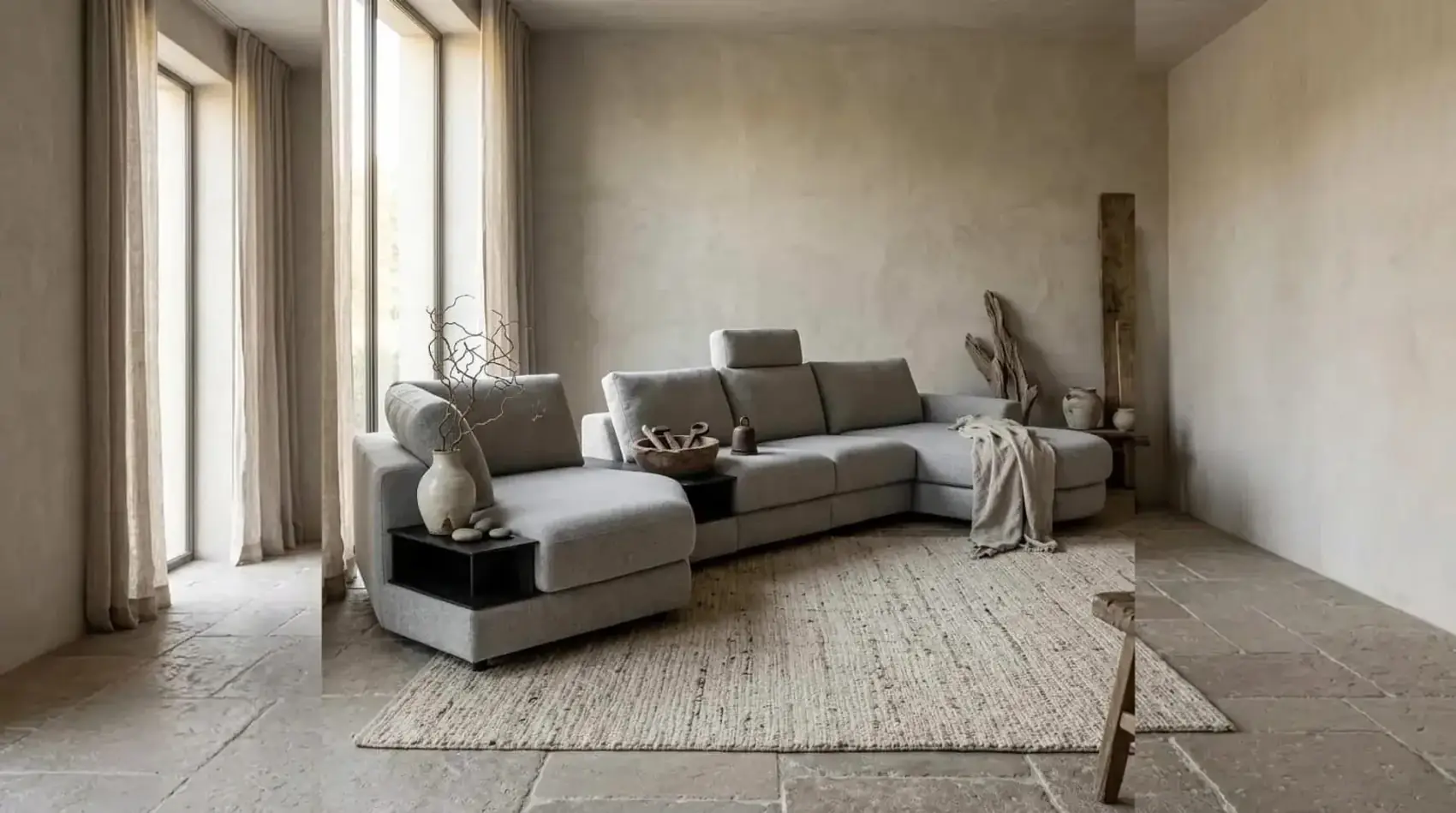 Graues Ecksofa Mirable mit Recamiere und schwarzem Zwischentisch vor einer verputzten Wand auf einem Juteteppich
