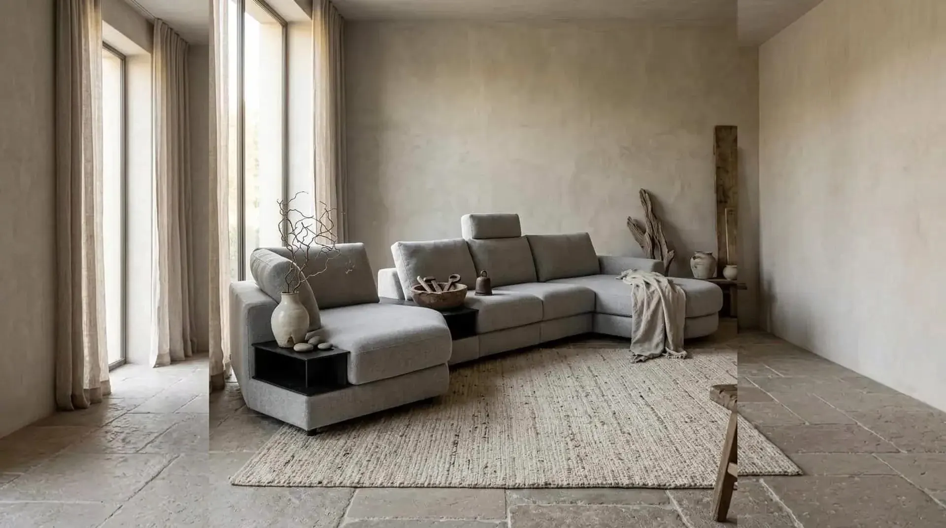 Graues Ecksofa Mirable mit Recamiere und schwarzem Zwischentisch vor einer verputzten Wand auf einem Juteteppich